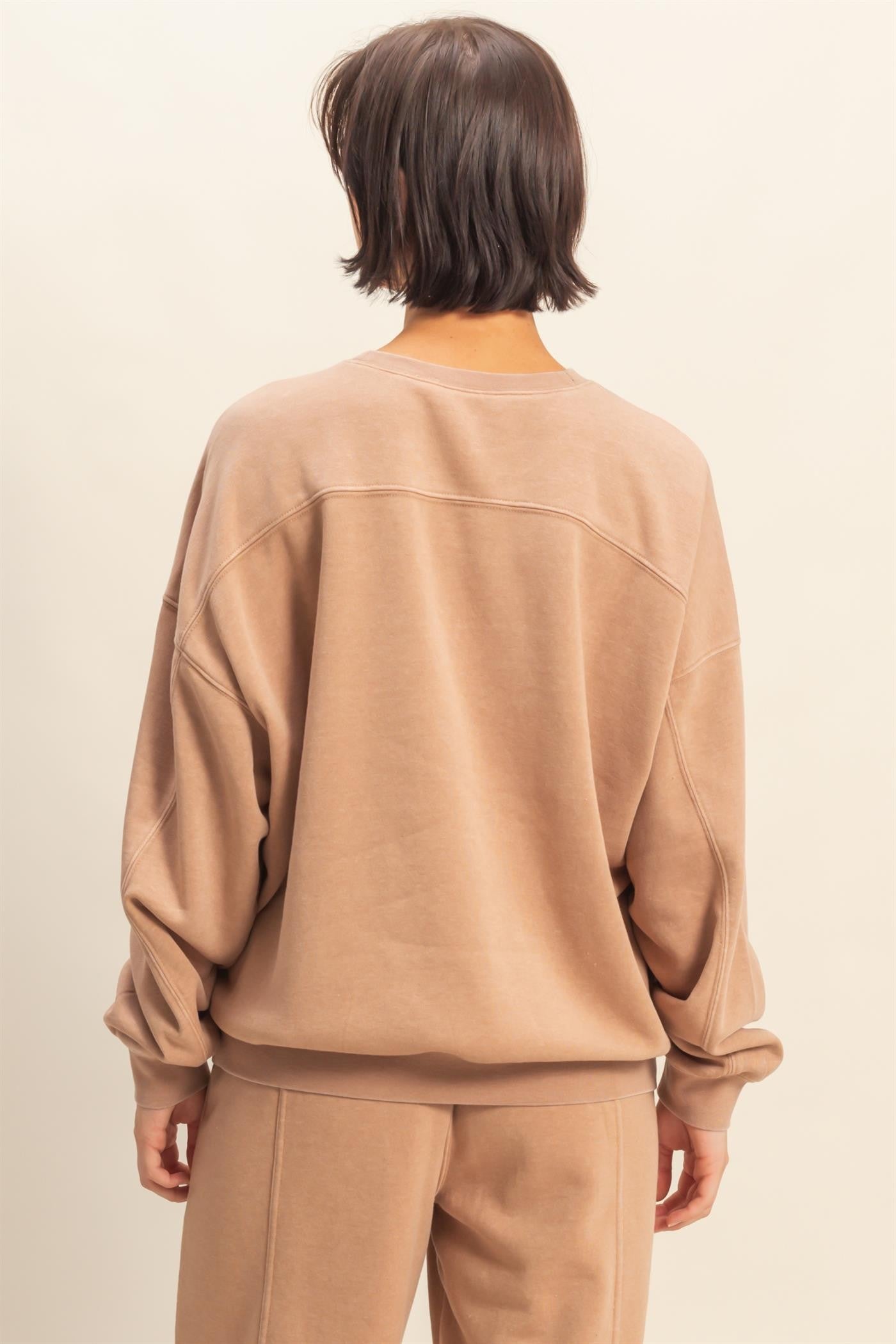 woman wearing a taupe oversized sweatshirt with dropped shoulders and long sleeves, viewed from the back