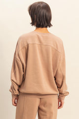 woman wearing a taupe oversized sweatshirt with dropped shoulders and long sleeves, viewed from the back