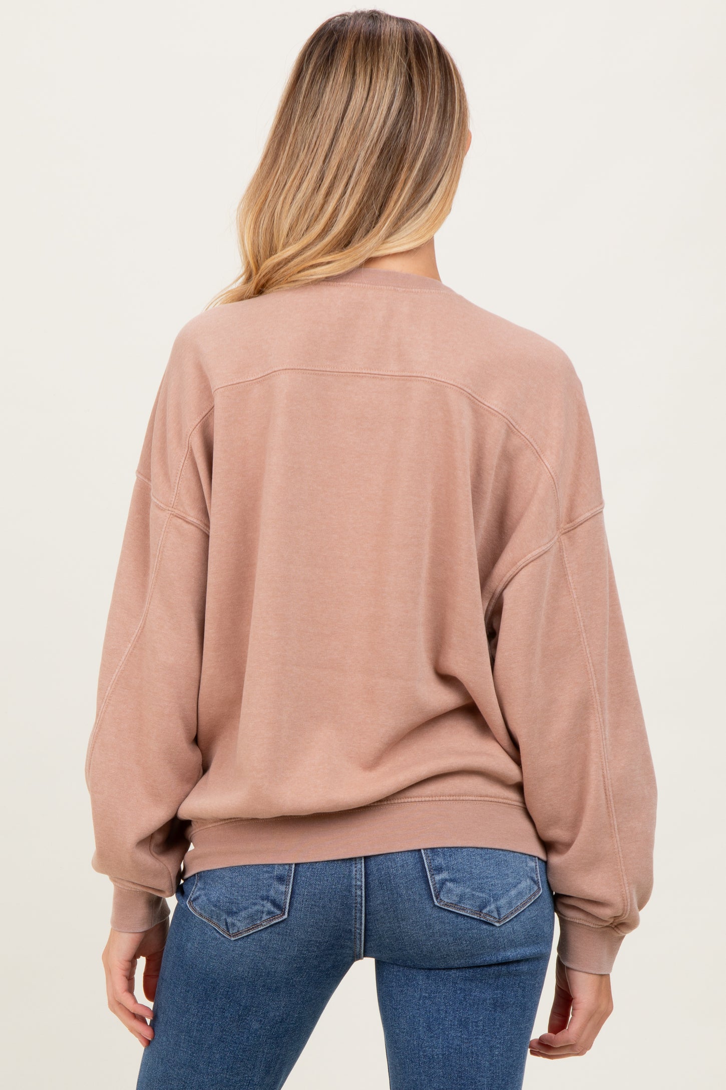 woman wearing a relaxed fit blush pink maternity sweatshirt from the back, paired with blue jeans