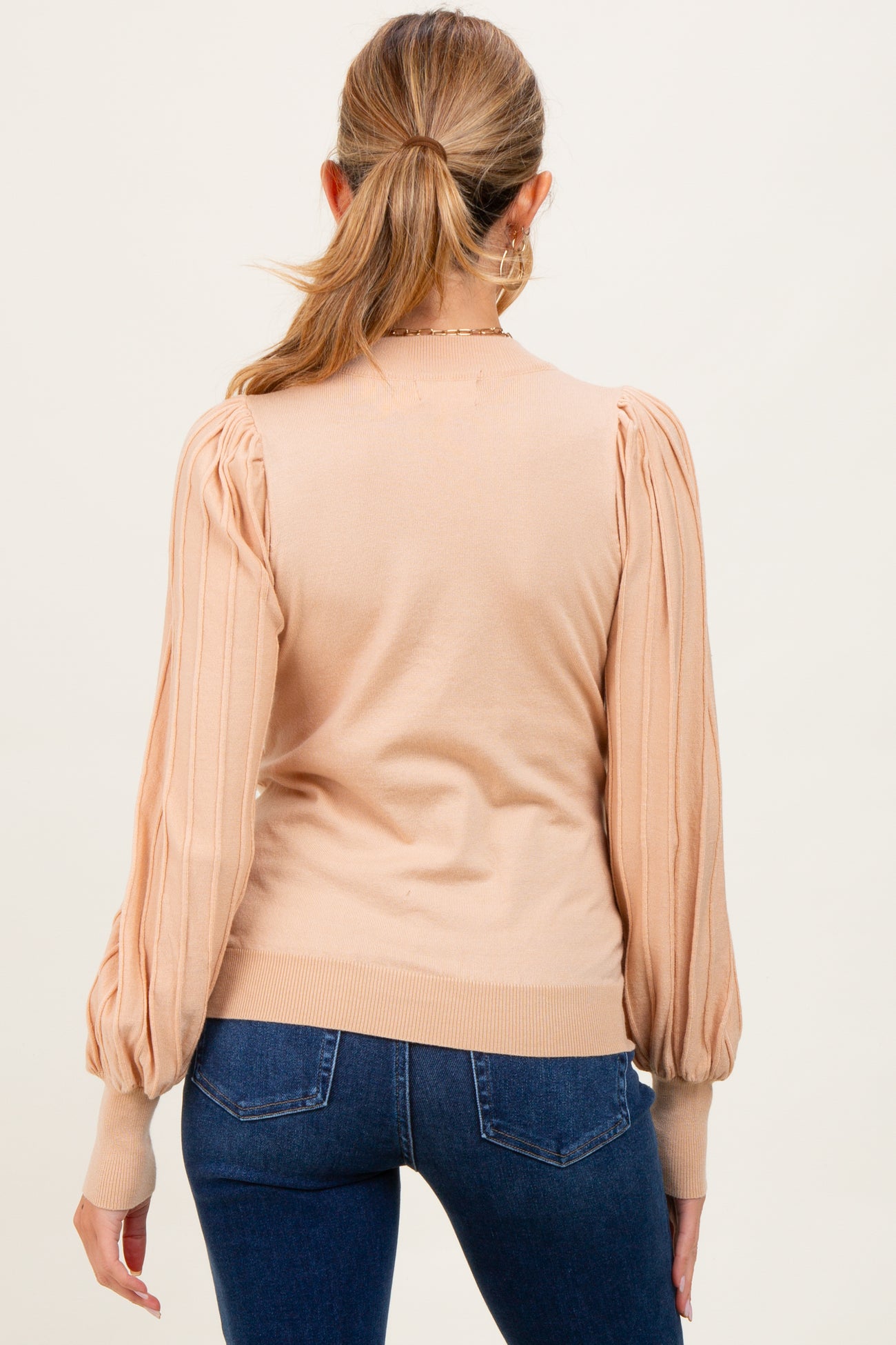 woman wearing a beige maternity sweater with puffed sleeves and ribbed cuffs, viewed from the back