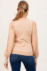 woman wearing a beige maternity sweater with puffed sleeves and ribbed cuffs, viewed from the back