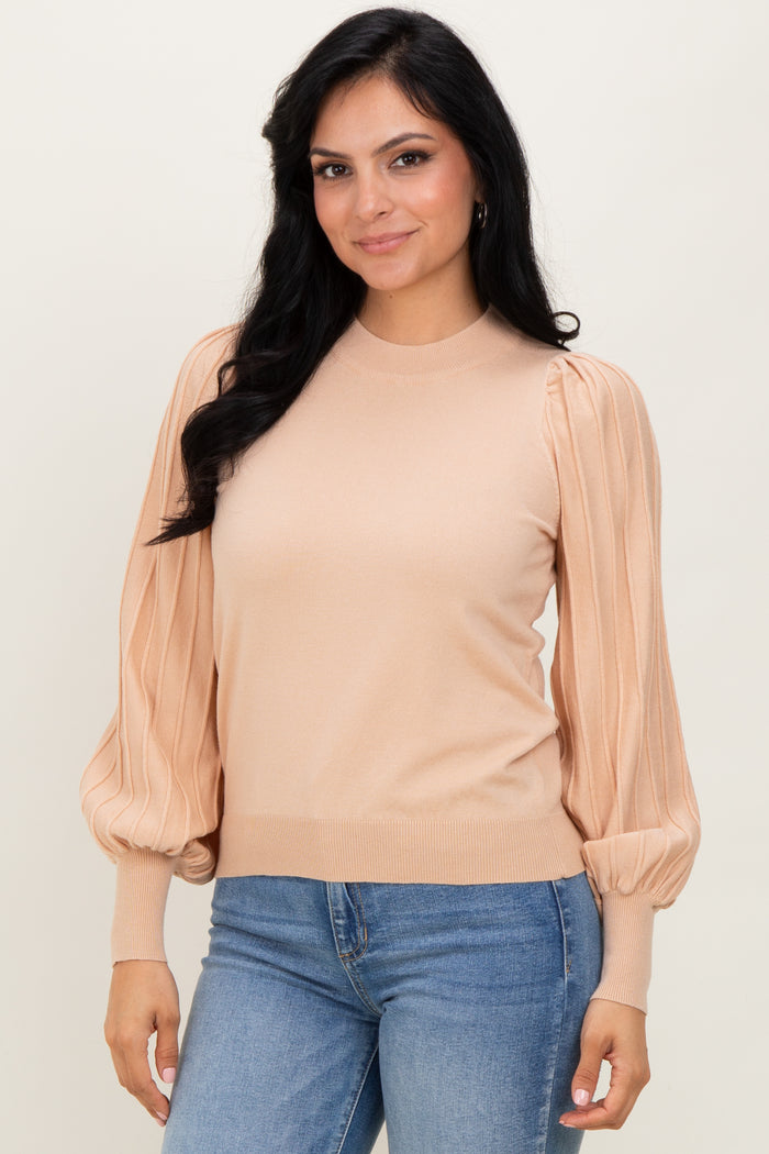 woman wearing a beige sweater with puffed sleeves, paired with blue jeans, smiling at the camera