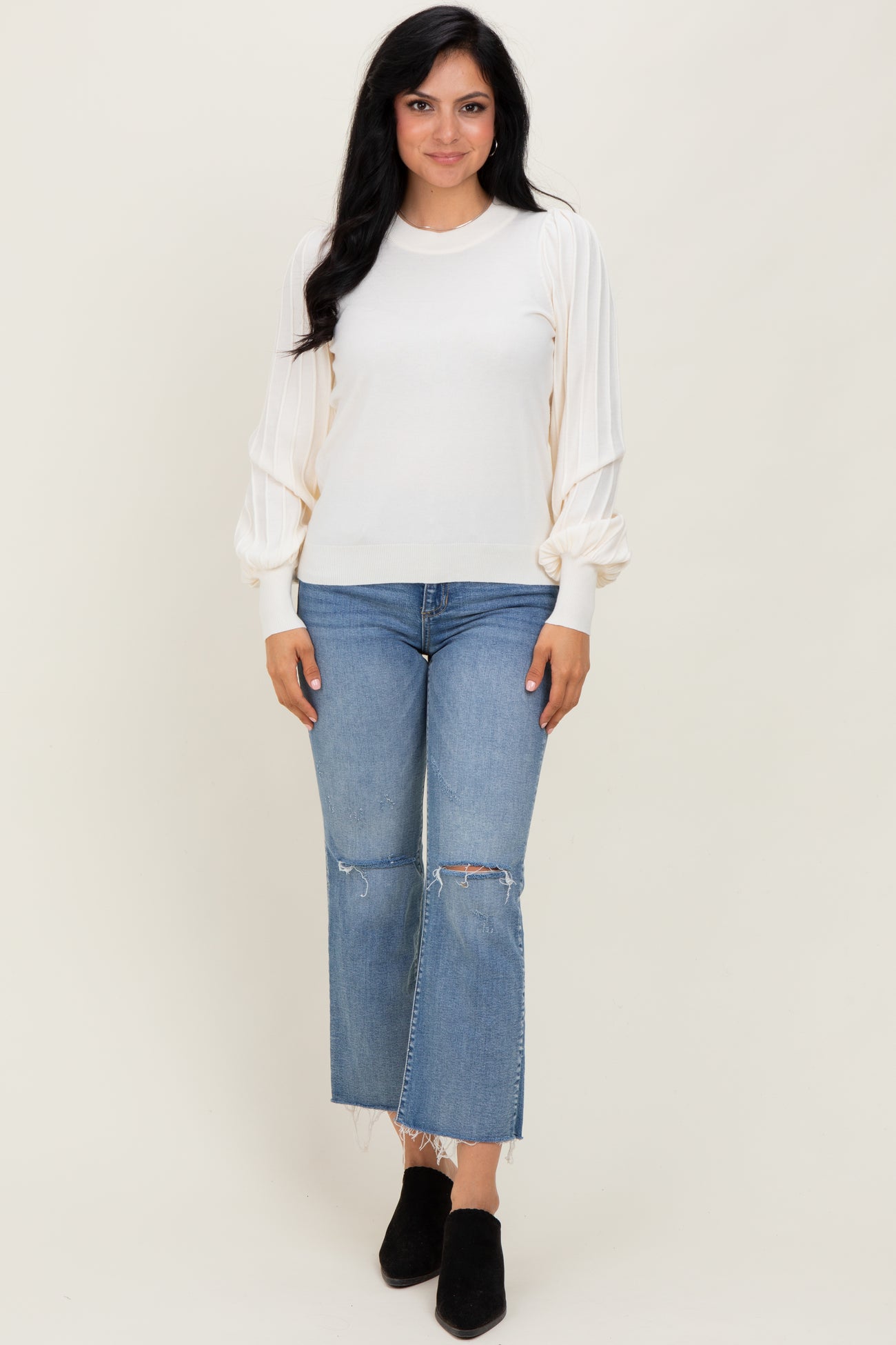 woman wearing a cream long sleeve sweater with puff sleeves and paired with distressed light blue cropped jeans