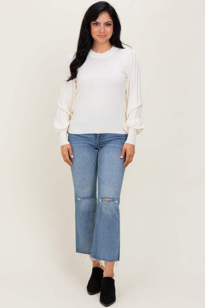 woman wearing a cream long sleeve sweater with puff sleeves and paired with distressed light blue cropped jeans