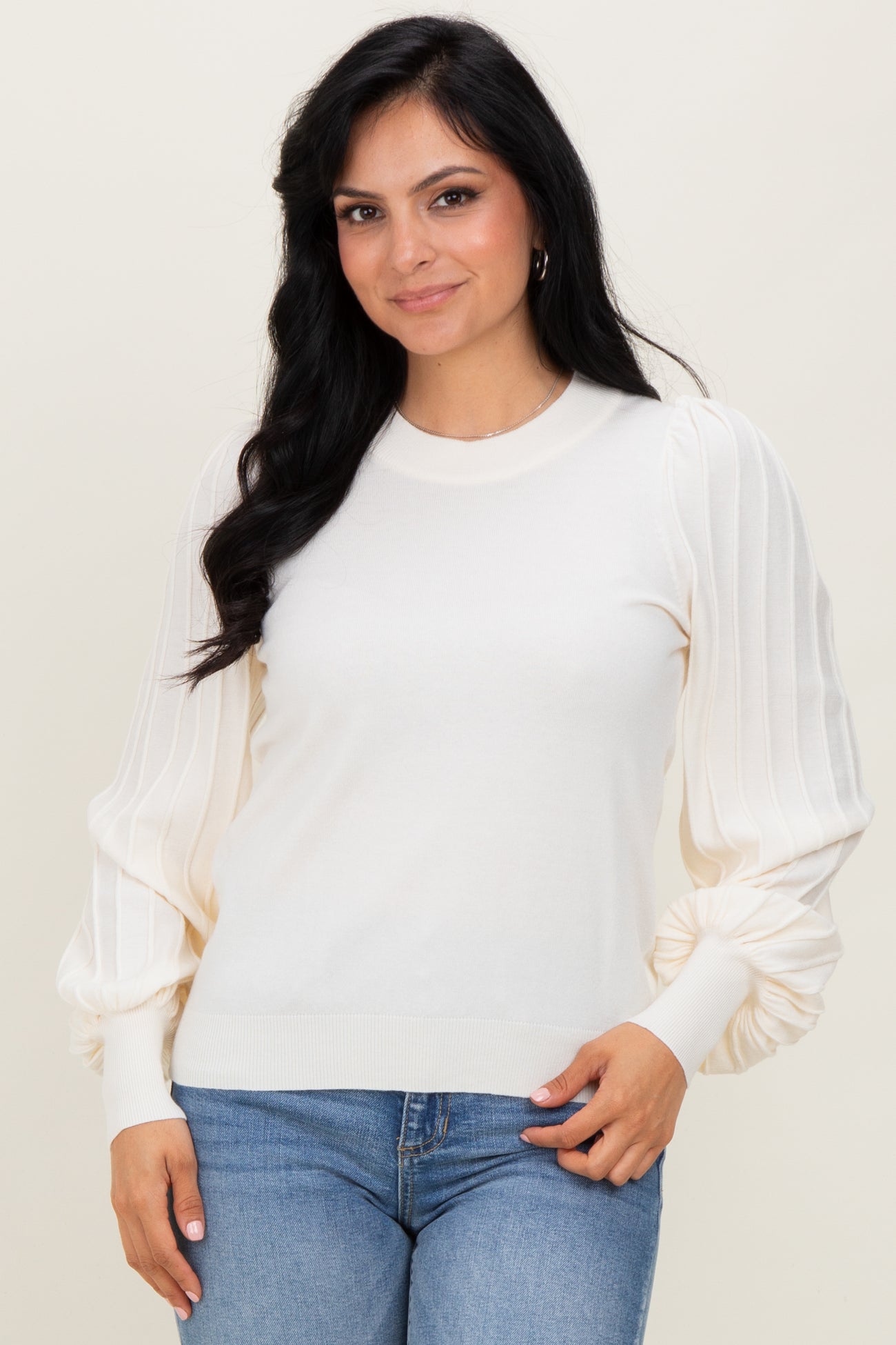 woman wearing a cream-colored sweater with puffed sleeves paired with blue jeans