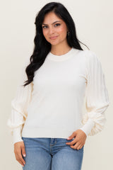 woman wearing a cream-colored sweater with puffed sleeves paired with blue jeans