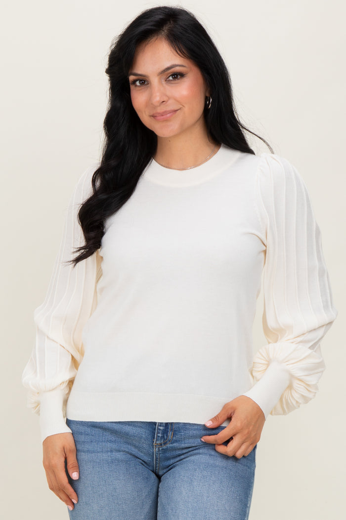 woman wearing a cream-colored sweater with puffed sleeves paired with blue jeans