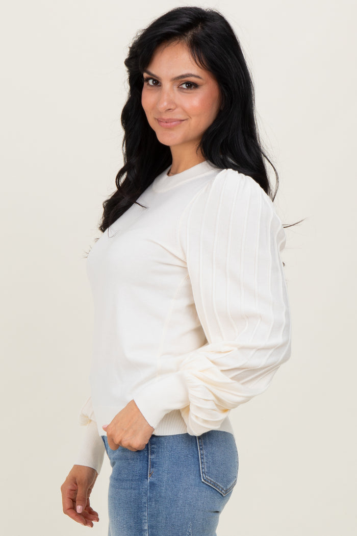 woman wearing a cream long sleeve top with puffed sleeves and fitted cuffs, styled with blue jeans