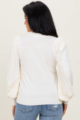 woman wearing a cream puff sleeve sweater with a fitted hem and back detail, paired with blue jeans
