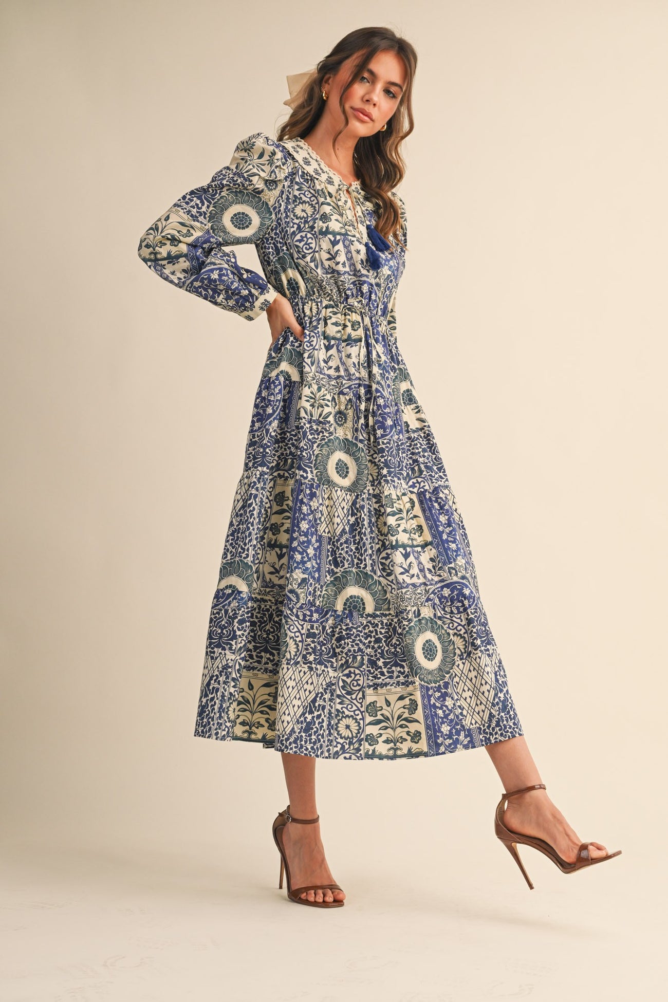 woman wearing a long sleeve blue and cream patterned maxi dress with a tiered design and a cinched waist