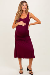 woman wearing a burgundy maternity dress with a fitted bodice and ruched detailing, showing her baby bump