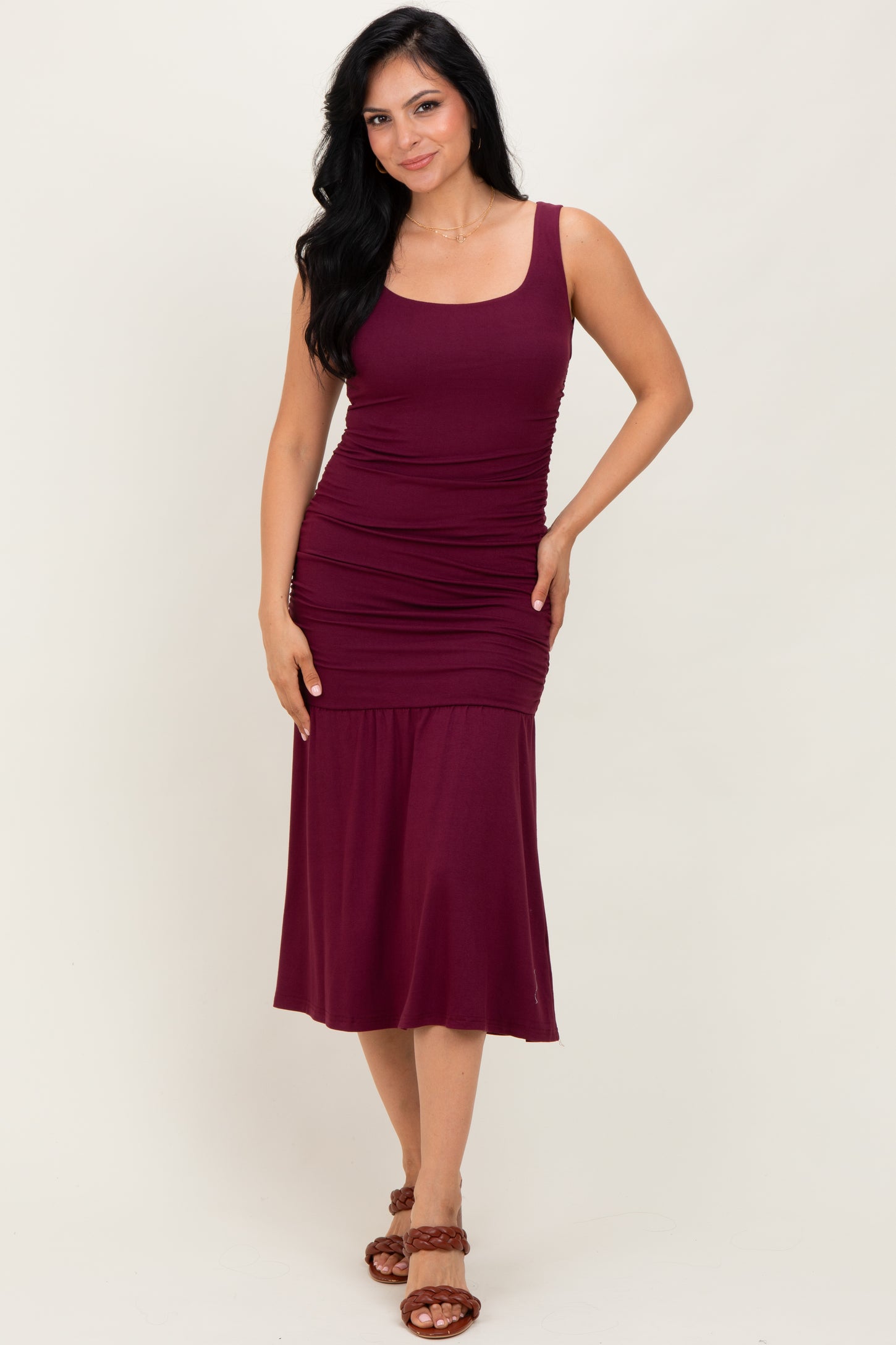 woman wearing a burgundy sleeveless ruched midi dress and brown strappy sandals