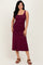 woman wearing a burgundy sleeveless midi dress with ruching details and standing with one hand on her hip