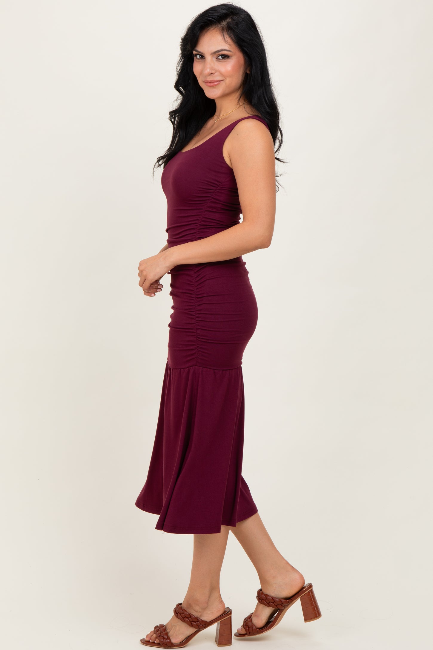woman wearing a burgundy fitted midi dress with ruching details and a flared hem, paired with brown heeled sandals