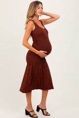 woman wearing a brown maternity dress with ruched details and a flowing skirt, cradling her baby bump