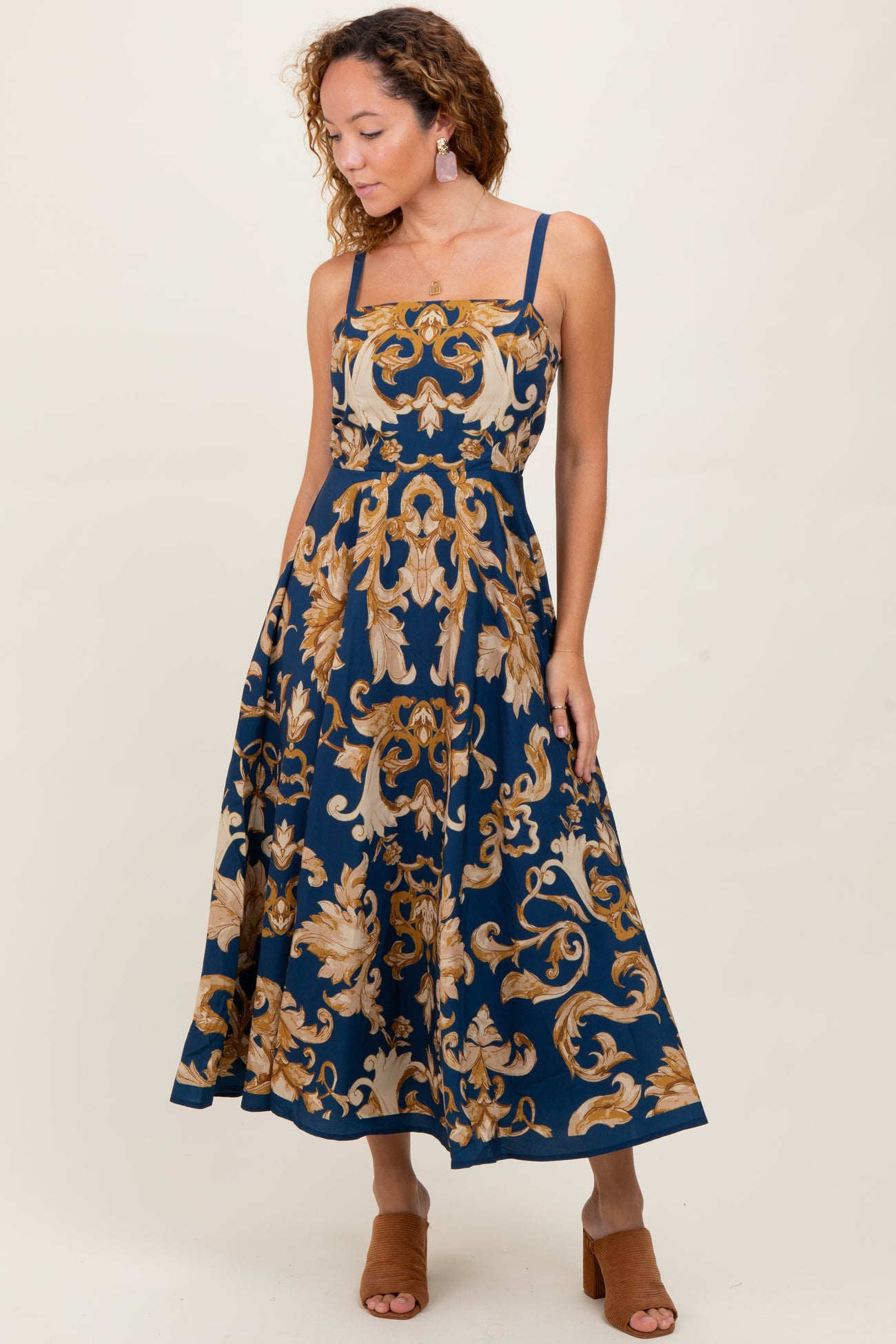 woman wearing a navy blue floral midi dress with spaghetti straps and a fitted bodice, styled with heeled sandals