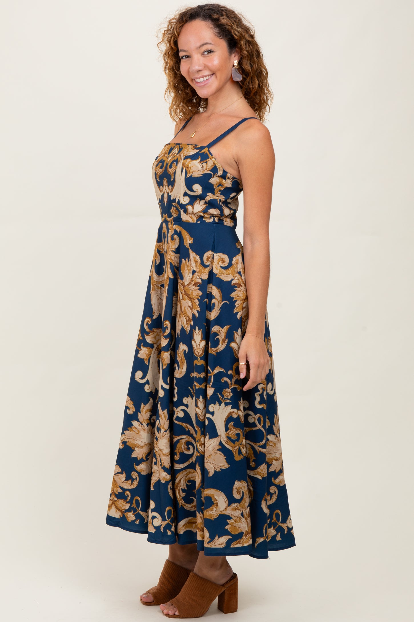 woman wearing a navy blue floral maxi dress with gold patterns and spaghetti straps, smiling with curly hair
