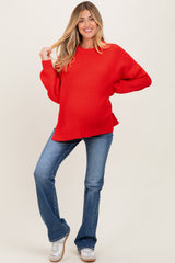 woman wearing a red oversized maternity sweater and flared jeans, showing her baby bump and smiling