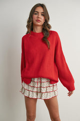 woman wearing a red oversized knitted sweater and a white floral ruffled skirt