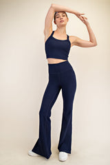 woman wearing a navy blue cropped tank top and flared leggings, posing with one arm raised
