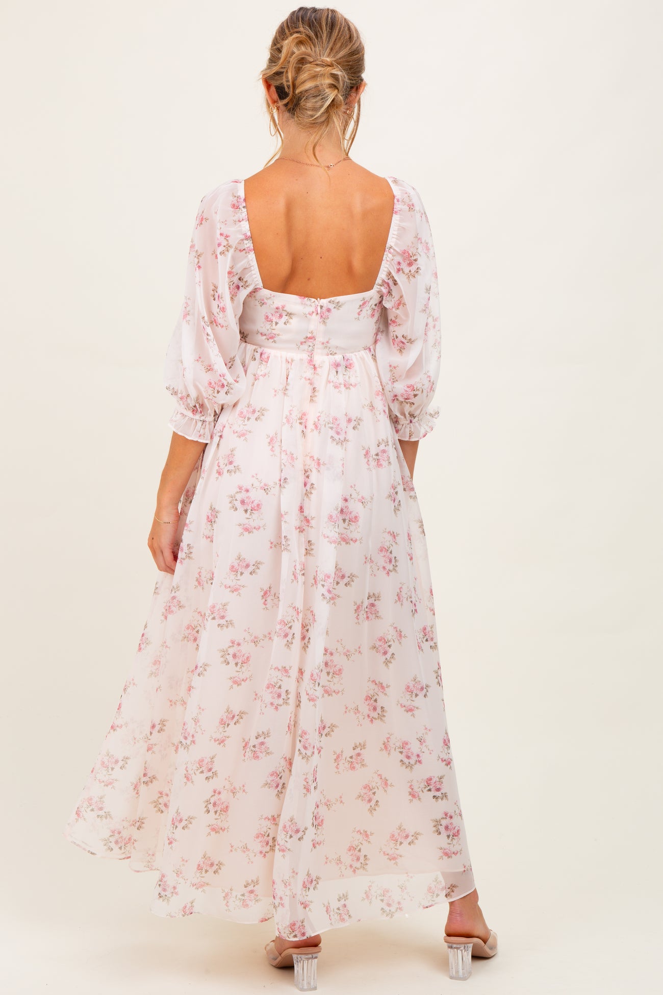 woman wearing a floral maternity maxi dress with puff sleeves and a low back, showing a baby bump