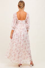 woman wearing a floral maternity maxi dress with puff sleeves and a low back, showing a baby bump
