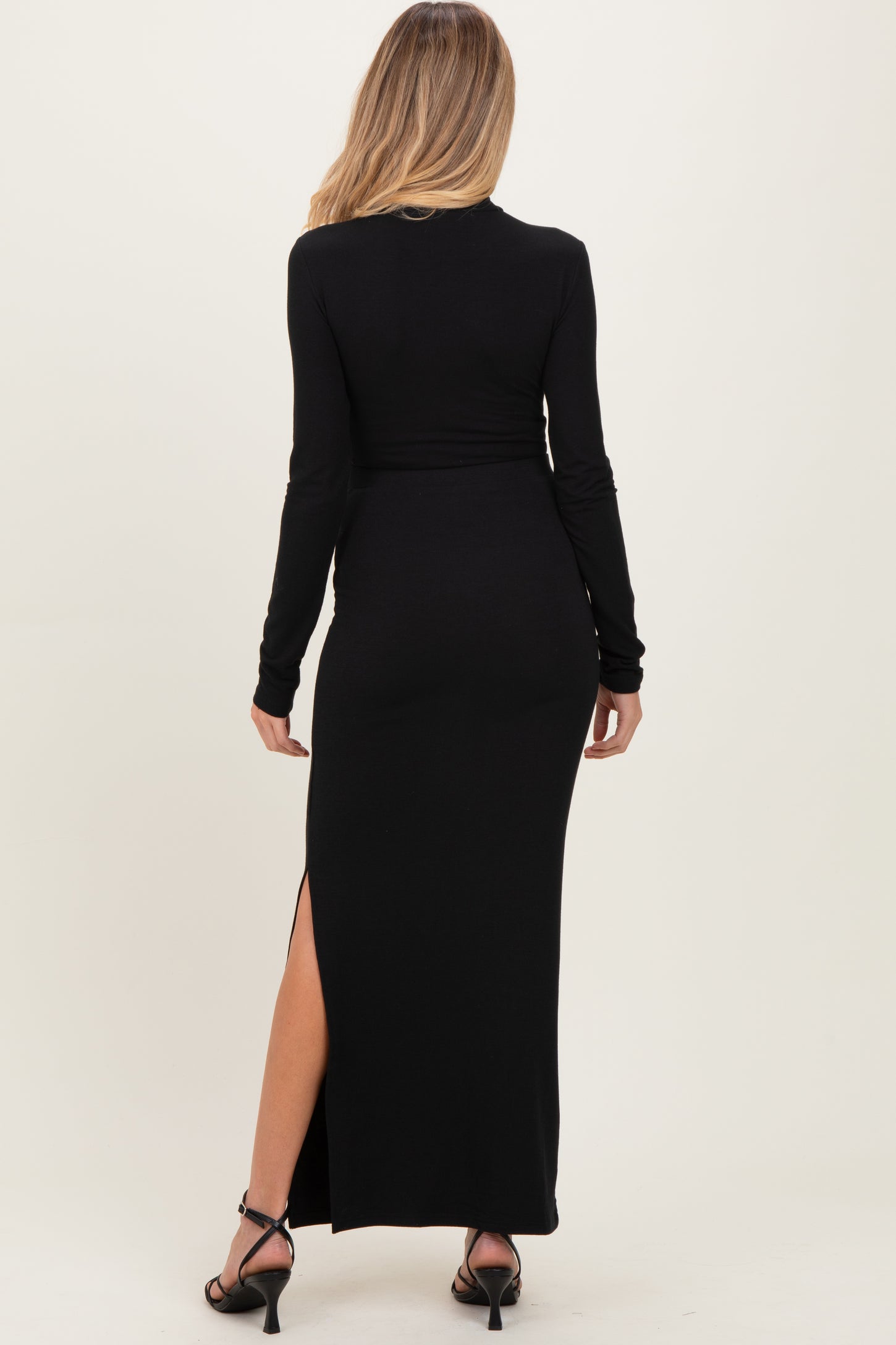 woman wearing a black long sleeve maternity dress with a side slit, viewed from the back