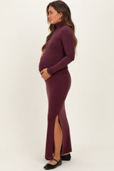 woman wearing a burgundy fitted maternity dress with a high neck and side slit, holding her baby bump