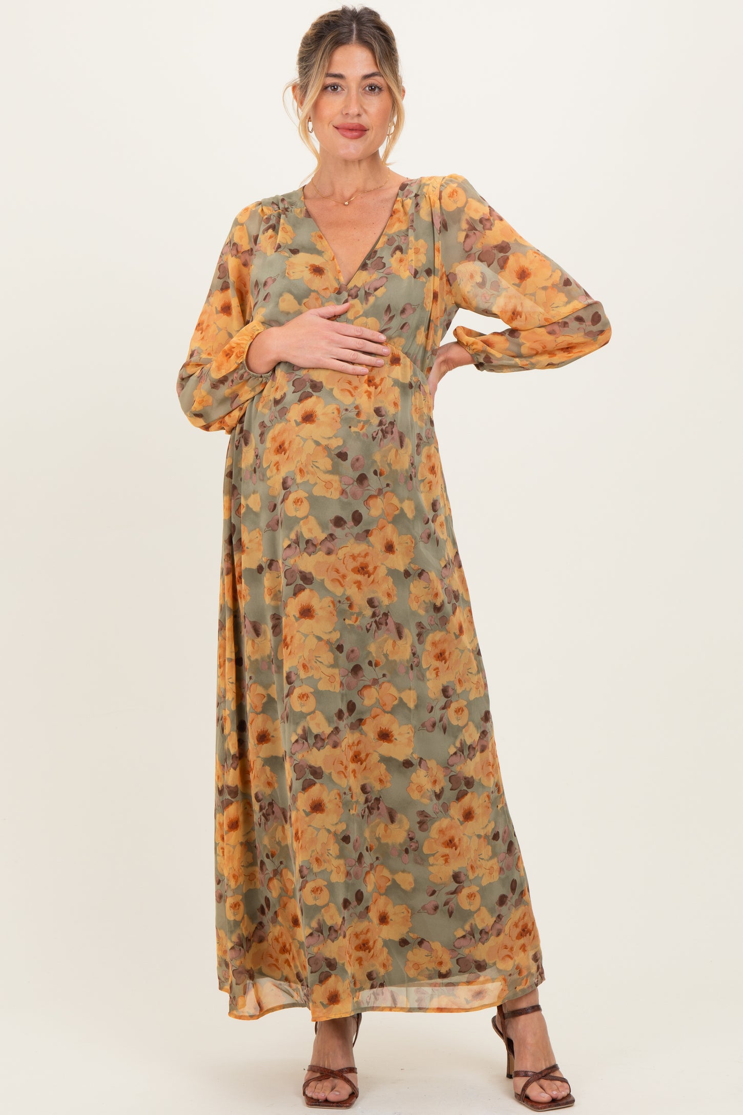 woman wearing a floral maternity maxi dress in earthy tones, holding her baby bump
