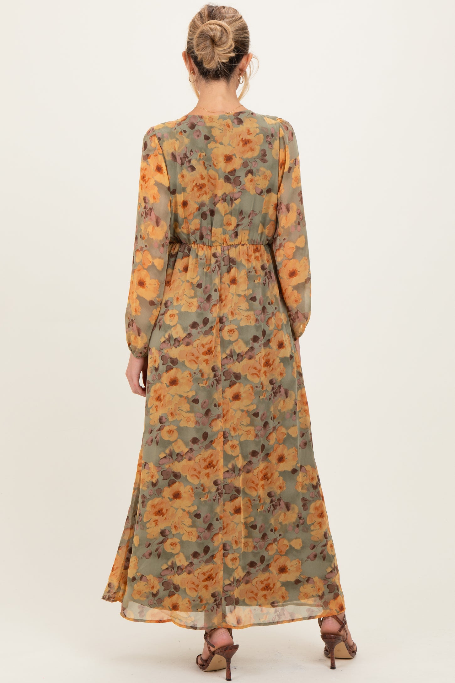 woman wearing a flowy floral maternity maxi dress in shades of green and orange, with long sleeves and a cinched waist