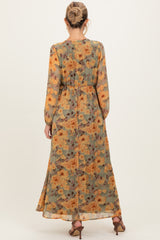 woman wearing a flowy floral maternity maxi dress in shades of green and orange, with long sleeves and a cinched waist