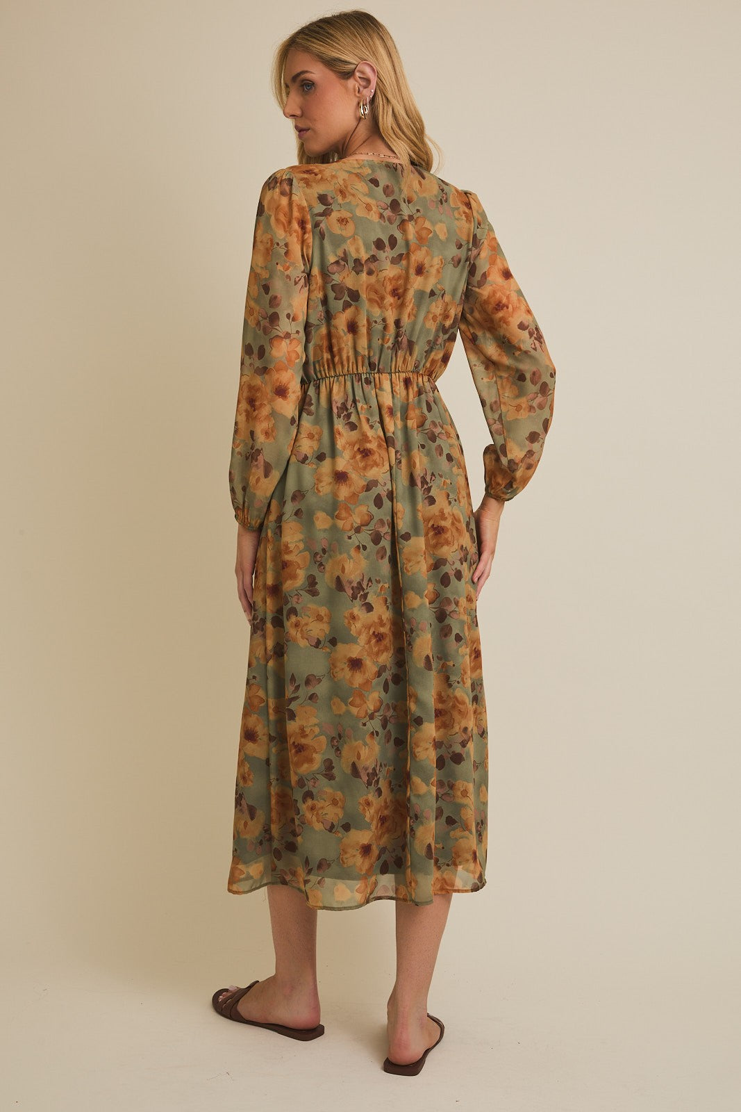woman wearing a floral patterned long sleeve maxi dress in olive green and mustard yellow, showing the back view