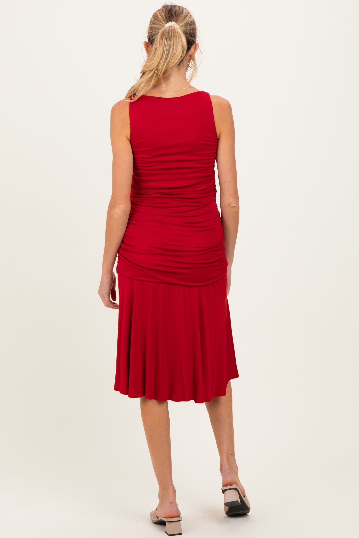 woman wearing a red sleeveless maternity dress with gathered detailing and a flared skirt, showing a baby bump from the back