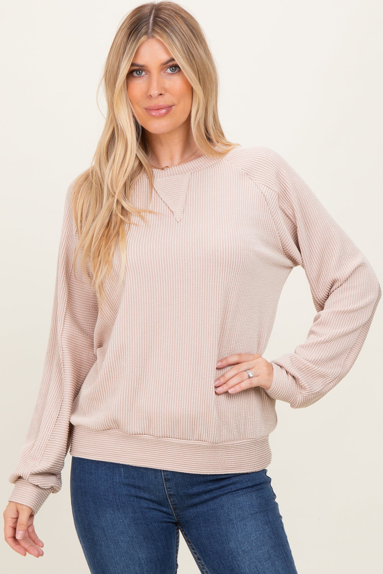 woman wearing a beige ribbed long sleeve sweatshirt with a relaxed fit and drop shoulder seams paired with jeans