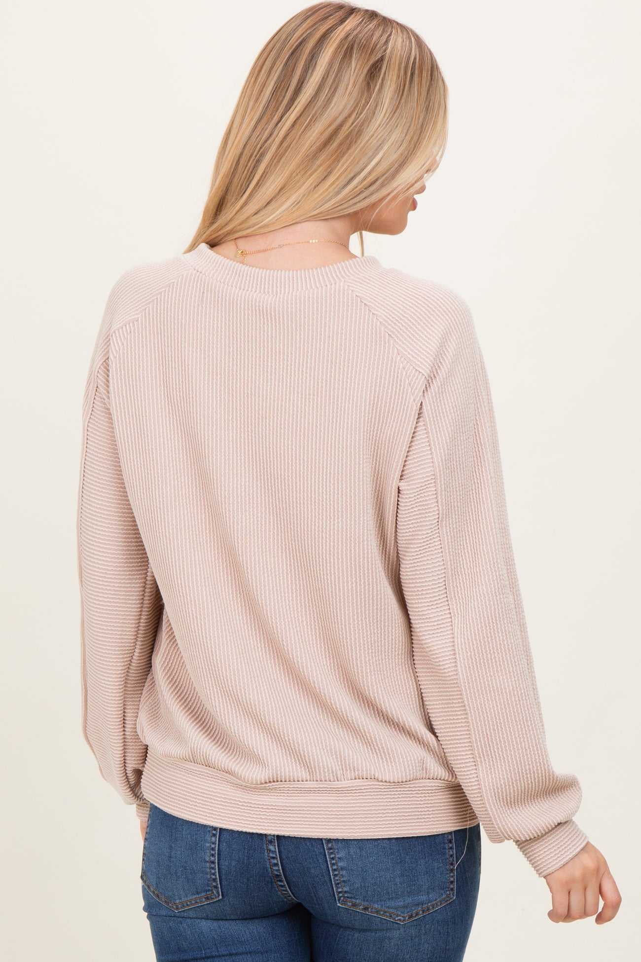 woman wearing a light pink ribbed sweater with long sleeves and a relaxed fit, viewed from the back