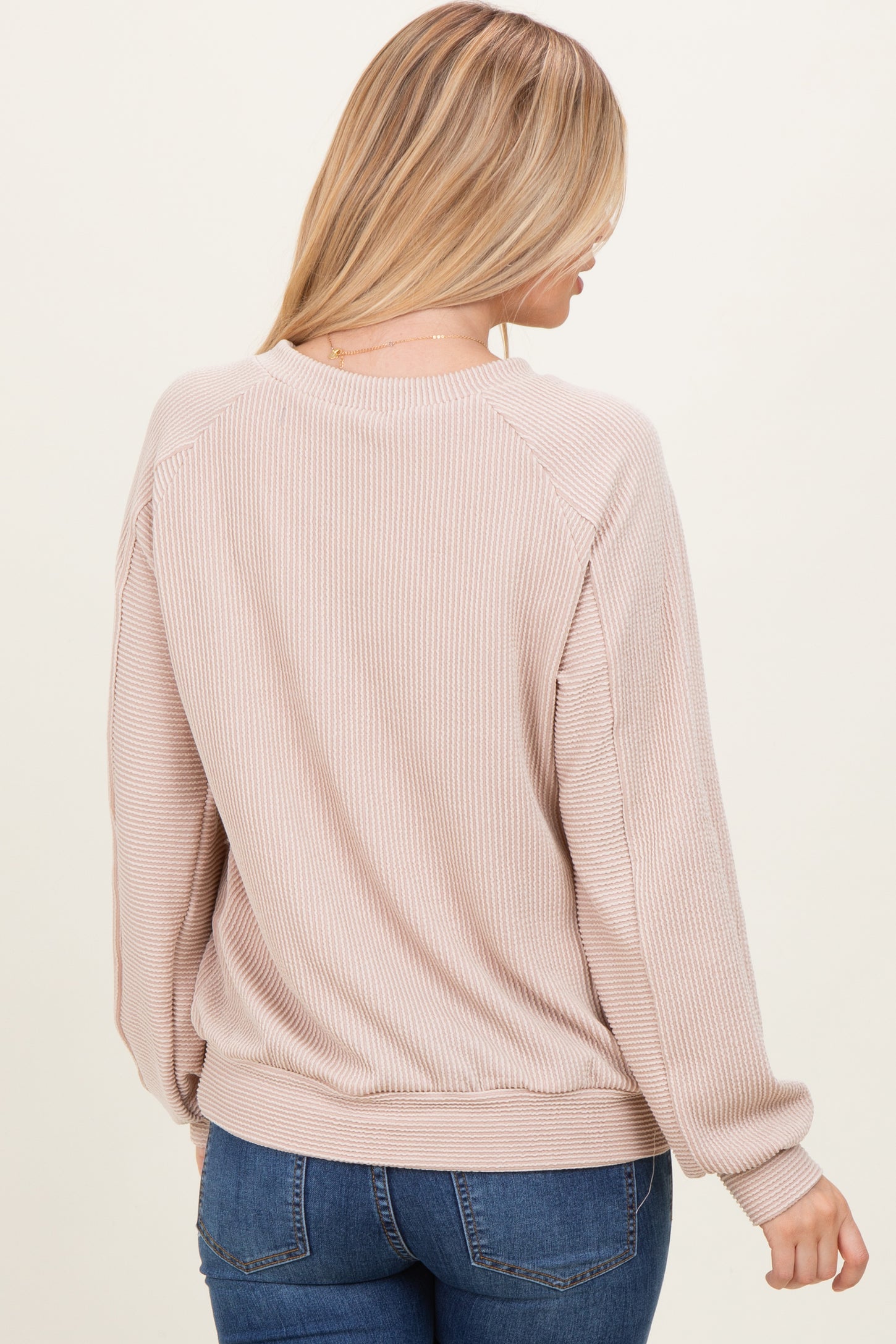 woman wearing a light pink ribbed sweater with long sleeves and a relaxed fit, viewed from the back