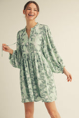 woman wearing a green floral long sleeve mini dress with a gathered skirt and tie detail at the neckline
