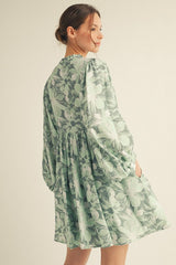 woman wearing a green floral print mini dress with puff sleeves and a gathered back detail