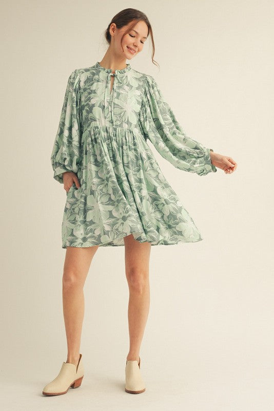 woman wearing a green floral long sleeve dress with a high neckline and pockets, styled with ankle boots