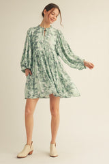 woman wearing a green floral long sleeve dress with a high neckline and pockets, styled with ankle boots
