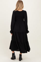 woman wearing a black maternity maxi dress with long sleeves and tiered skirt, showing a smocked bodice from the back