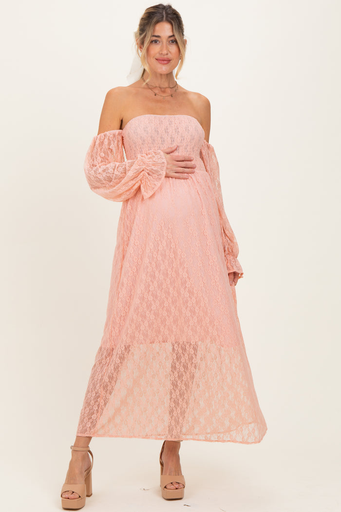 woman wearing a peach off-the-shoulder lace maternity dress and holding her baby bump