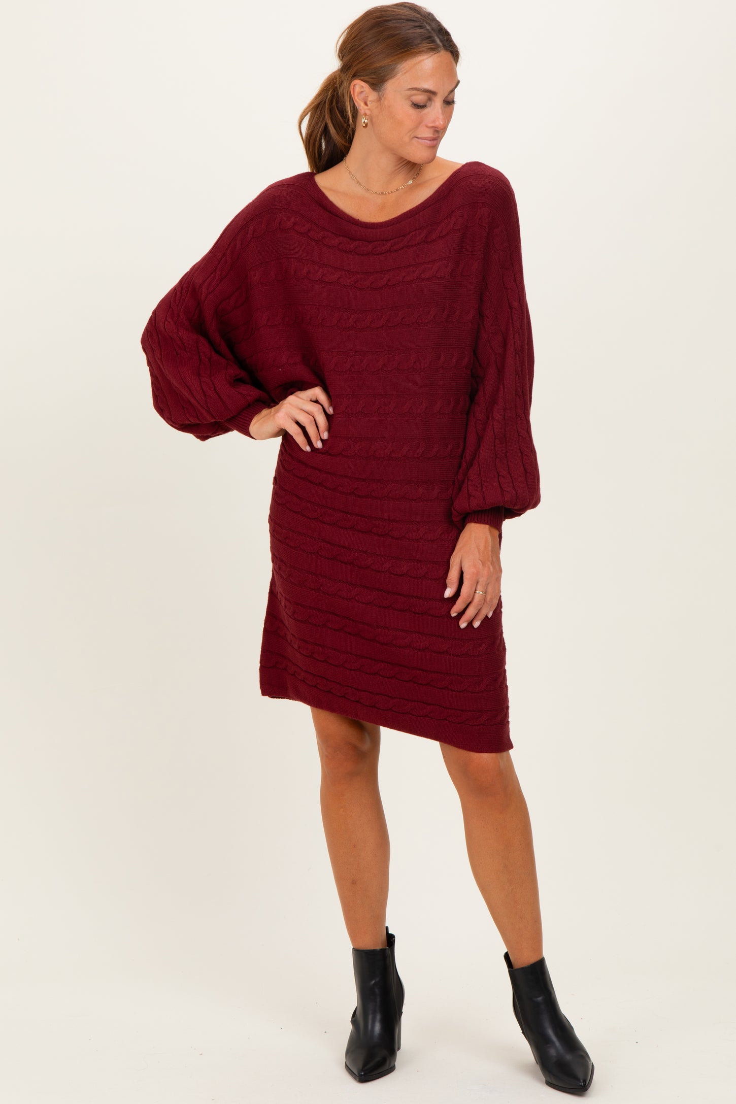 woman wearing a burgundy oversized knit dress with balloon sleeves, styled with ankle booties