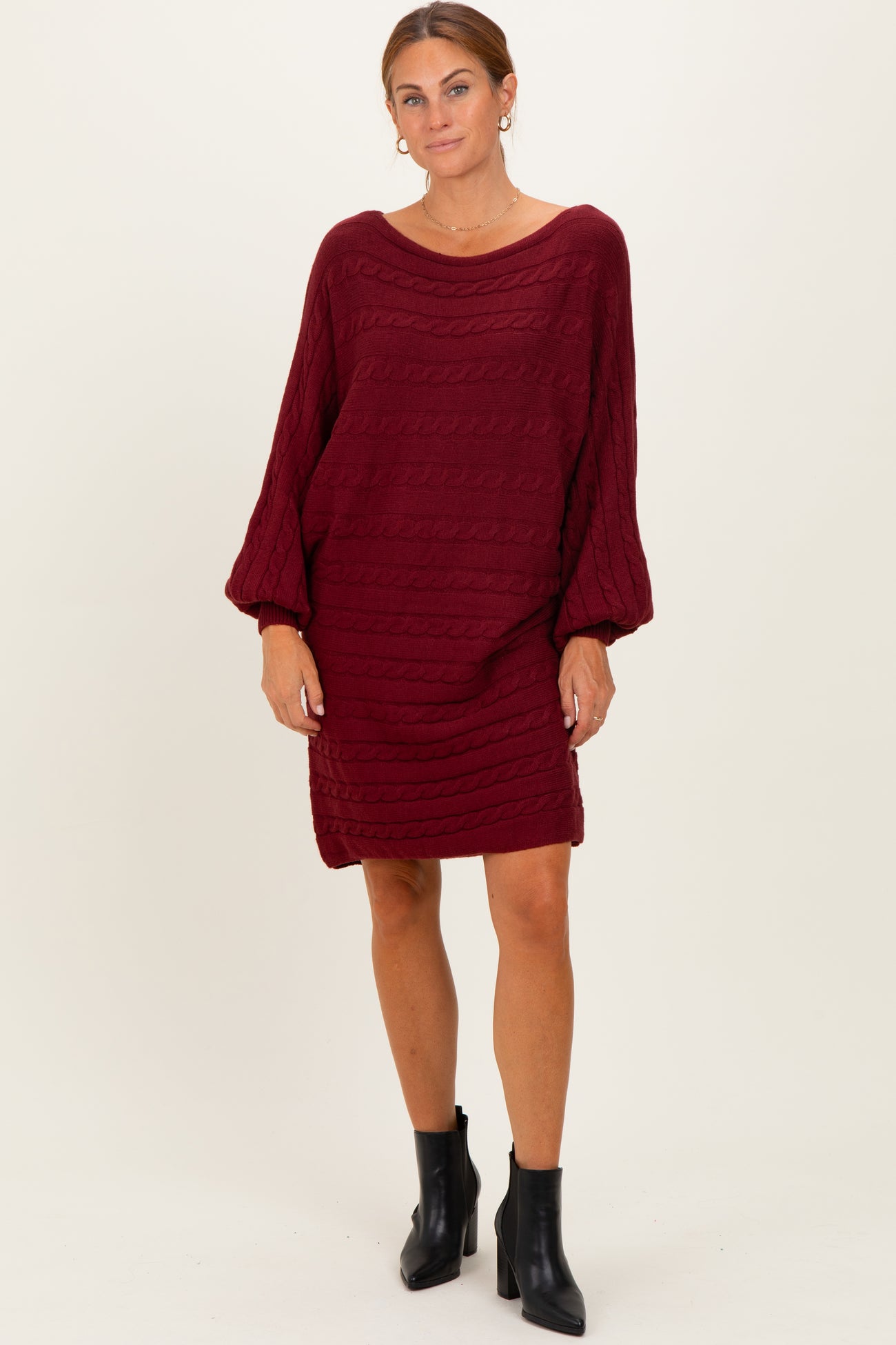 woman wearing a burgundy cable knit sweater dress with balloon sleeves and black ankle boots