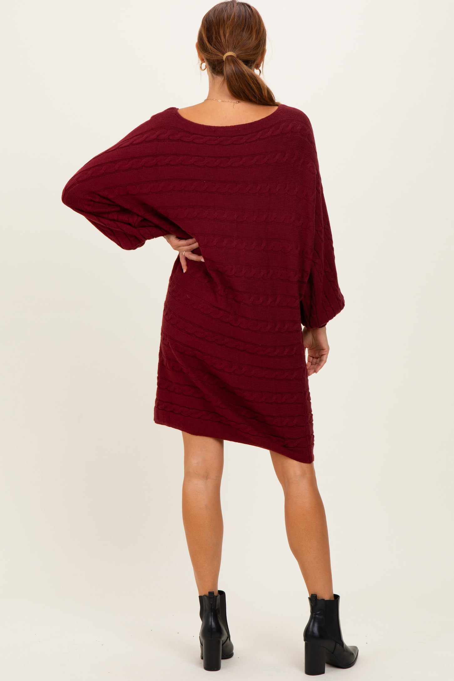 woman wearing a burgundy oversized cable knit sweater dress with long sleeves and a relaxed fit, facing away from the camera
