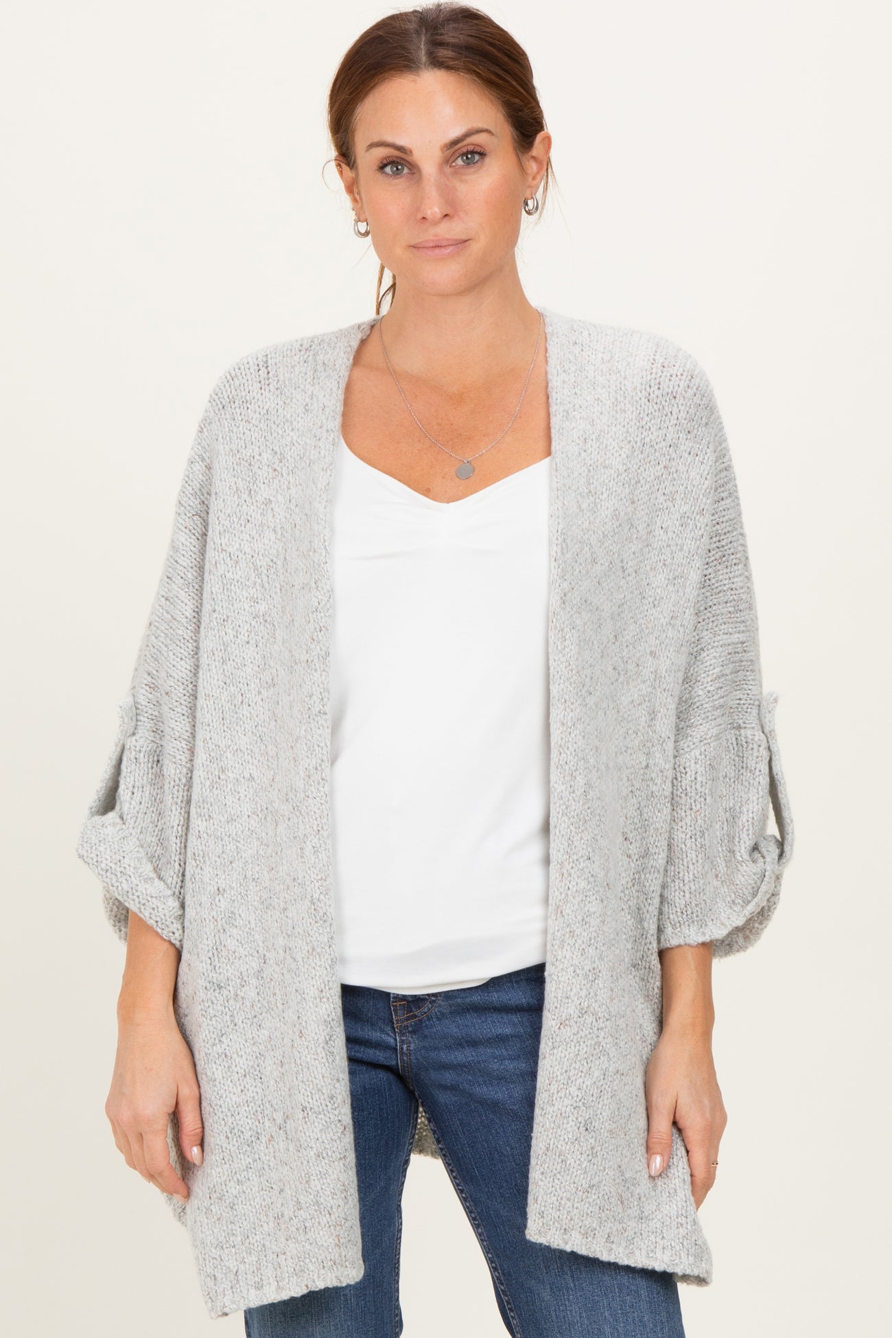 woman wearing a light gray cardigan with rolled sleeves over a white top and dark jeans