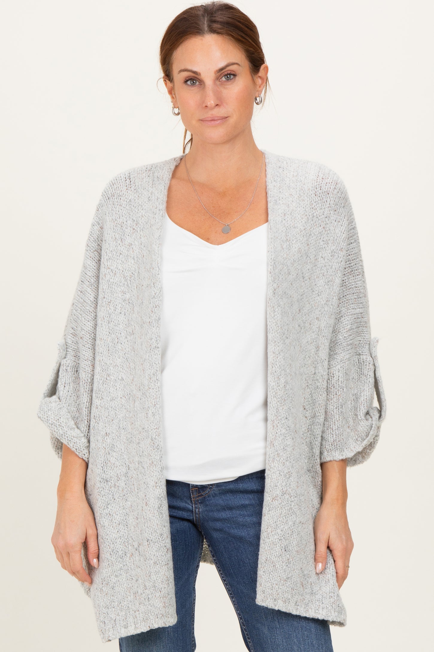 woman wearing a light gray cardigan with rolled sleeves over a white top and dark jeans