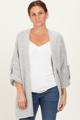woman wearing a light gray open-knit cardigan over a white v-neck top with rolled-up sleeves and blue jeans