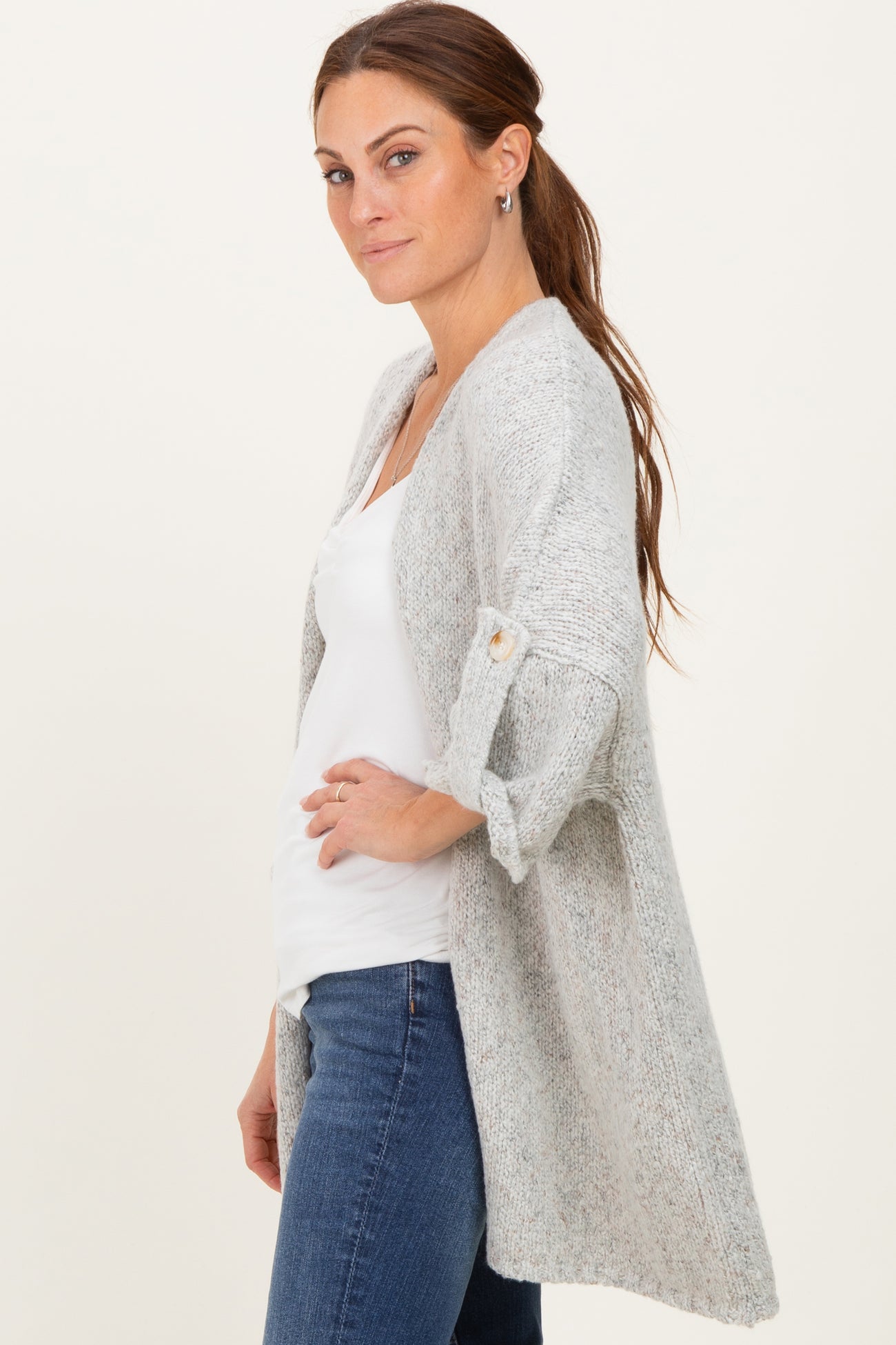 woman wearing a light gray open cardigan with rolled sleeves and a white top, styled with blue jeans