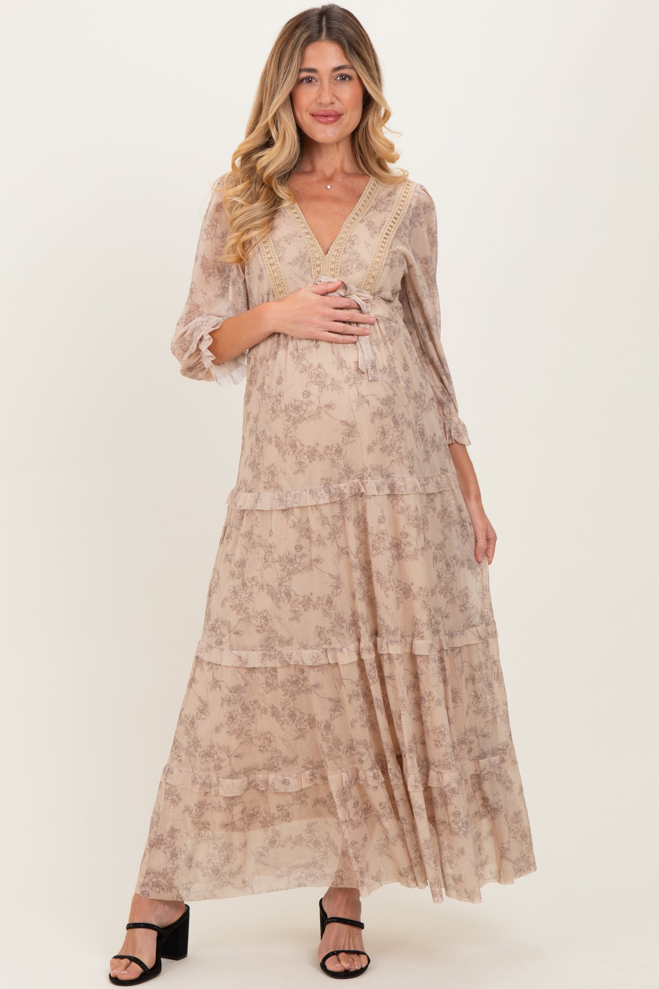 woman wearing a flowy beige floral maternity maxi dress with three-quarter sleeves and a visible baby bump